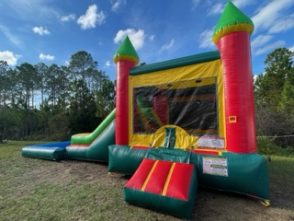 Side view of an inflatable bounce house and slide combo featuring bright green, yellow and red colors. The structure includes a large bounce area, a climbing wall, and a slide with a pool area at the bottom of the slide, with netted windows for visibility and airflow. Set up on a grassy lawn with trees in the background, the scene is lively and inviting, ideal for outdoor fun.