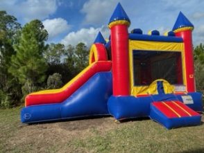 Bouncy castle with a large slide out the front of the bounce castle. There is a small slide out the side of the bounce castle. Bounce castle is red, blue and yellow.